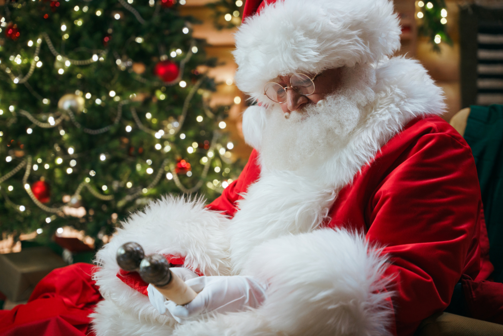 Santa Claus in a bright red costume with an ancient scroll in his hands against the Christmas tree